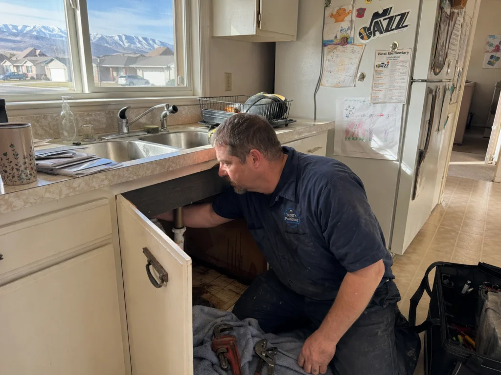 Licensed emergency plumber repairing a kitchen sink leak in a residential home to prevent water damage